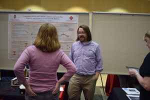 Two people discuss in front of the Biotechnology Center's poster "Using model systems and CRSPR to improve understanding, diagnosis, and treatment of cancer at UW-Madison."