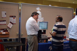 Two men talk in front of the Teledyne ISCO table. A large piece of equipment sits on the table in front of them.