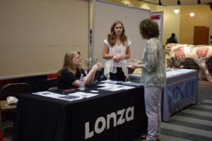 Three women talk at the Lonza and IDT tables.