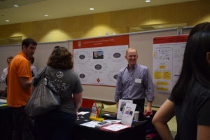 A group of people stand in front of the Biotechnology Center Core Services poster, and the man behind the table smiles at the camera.