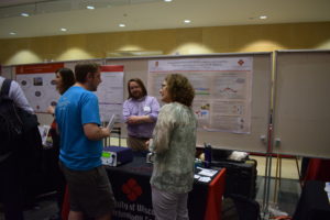A trio chats in front of the Biotechnology Center poster "Using model systems and CRISPR to improve understanding, diagnosis, and treatment of cancer at UW-Madison."