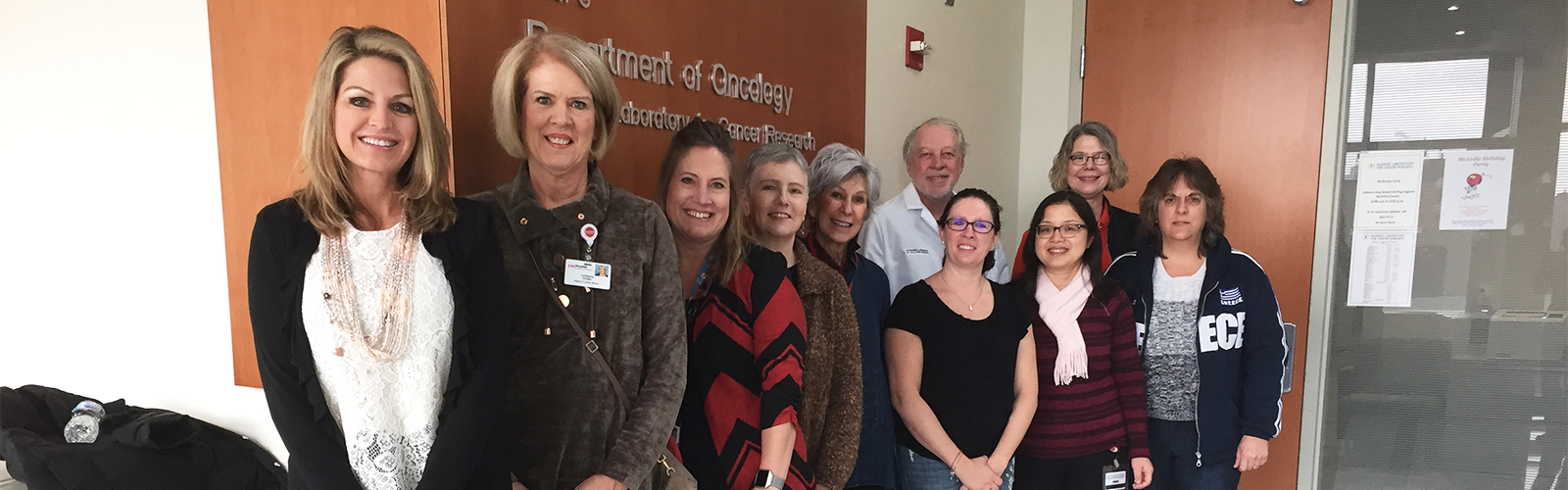 Ten BCRAN members tour McCardle Lab, pose for photo in front of sign saying Department of Oncology