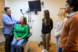 At left, Randall Kimple, professor of human oncology at the University of Wisconsin–Madison, examines patient Lisa Sutter while students Rachel Minne, Madalynn Wopat, and Saahil Javeri observe in a patient care room in the Wisconsin Institutes for Medical Research on April 15, 2025. Kimple is one of 10 recipients of the Award for Mentoring Undergraduates In Research, Scholarly and Creative Activities. Kimple works with undergraduates in his lab on cellular therapies to reverse radiation-induced damage to the salivary glands in patients with head and neck cancers. (Photo by Althea Dotzour / UW–Madison)